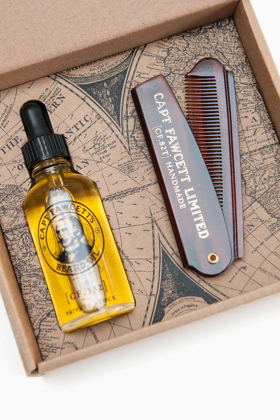 A grooming gift set in a brown cardboard box, featuring a bottle of beard oil and a folding comb with engraved branding.
