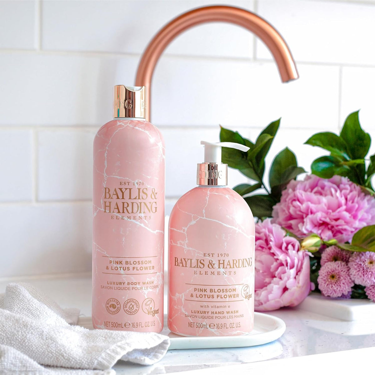 Two Baylis & Harding pink marble bottles on a kitchen counter with flowers in the background.