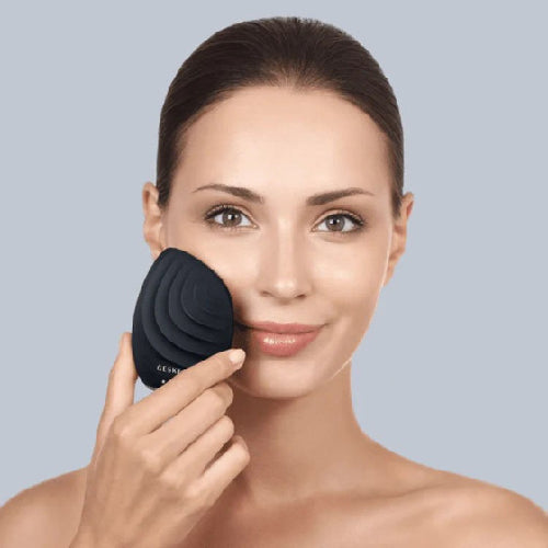 Woman using a black facial cleansing brush on a gray background