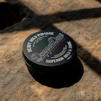 Black container of Dapper Dan Heavy Hold Pomade on a textured stone surface