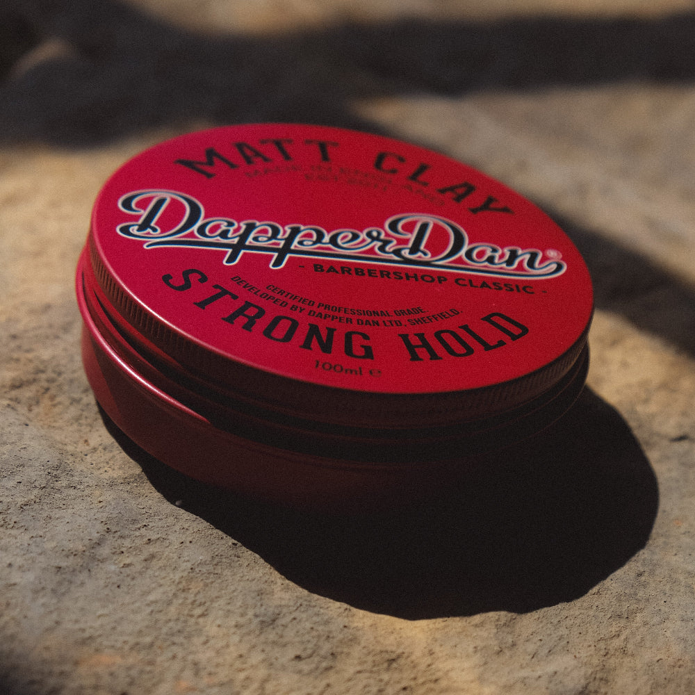 Red container of Dapper Dan Matt Clay Strong Hold hair product on a stone surface