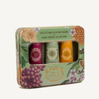 A rectangular metal gift set box labeled 'COLLECTION SOIN DES MAINS HAND CREAM COLLECTION' by Darjeeling Hand Creams, containing three hand creams visible through a clear window. The box is decorated with floral and botanical illustrations including grapes, honeycomb, and blossoms, on a light cream background.