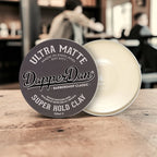 Dapper Dan Super Hold Clay container on a wooden surface with a blurred background