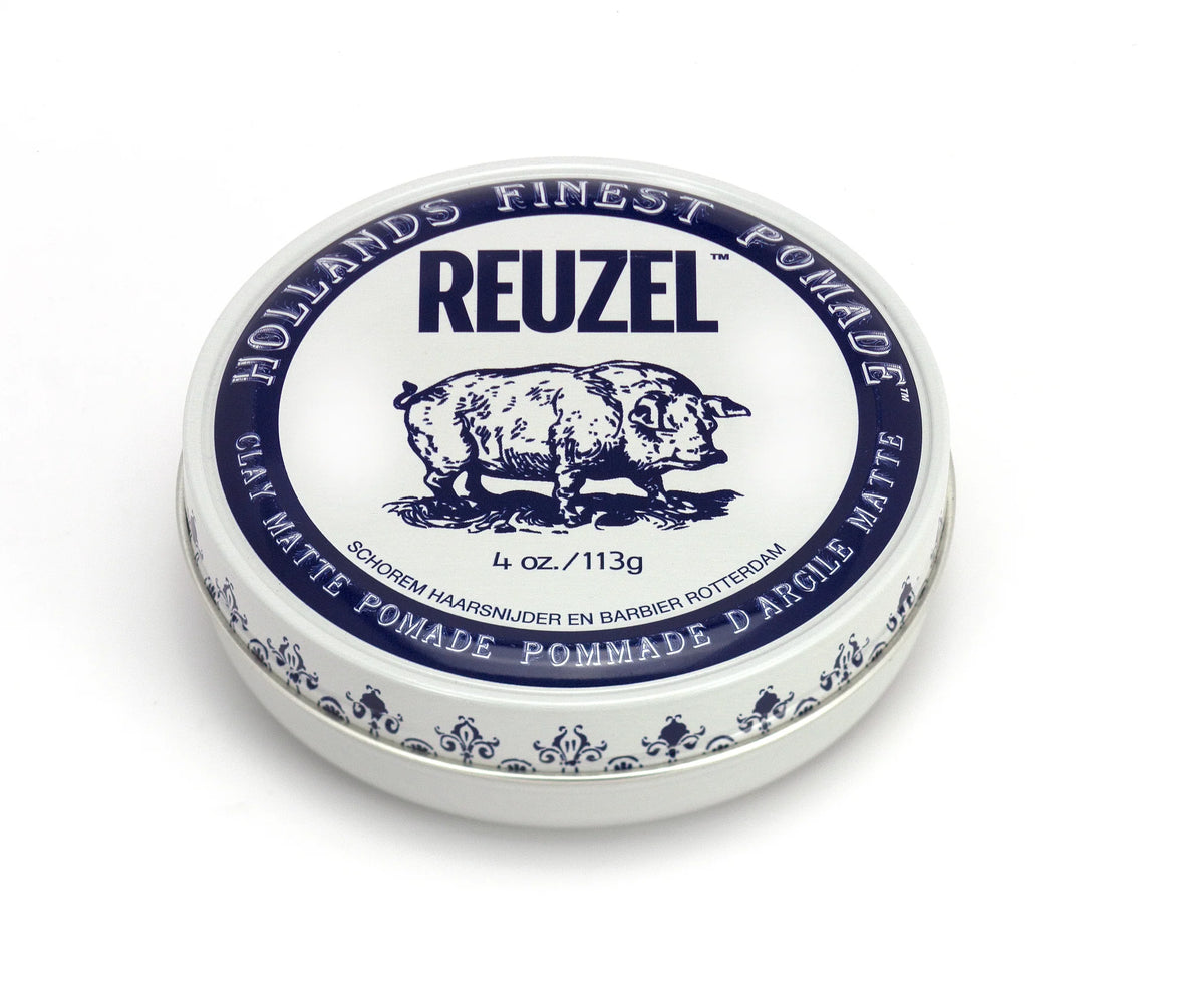 A round tin of Reuzel Holland's Finest Pomade in Clay Matte, featuring a white lid with a blue printed illustration of a pig and brand text, set against a plain white background.