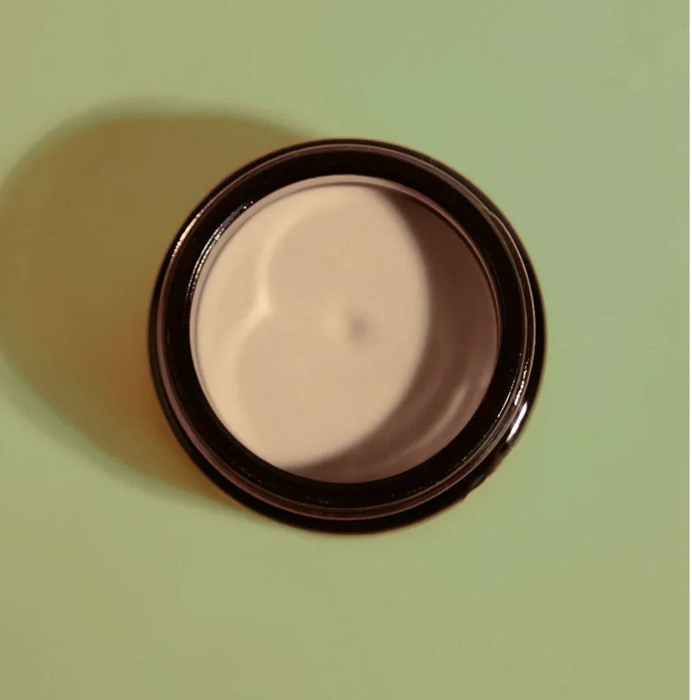 Cosmetic cream in a round container on a green background