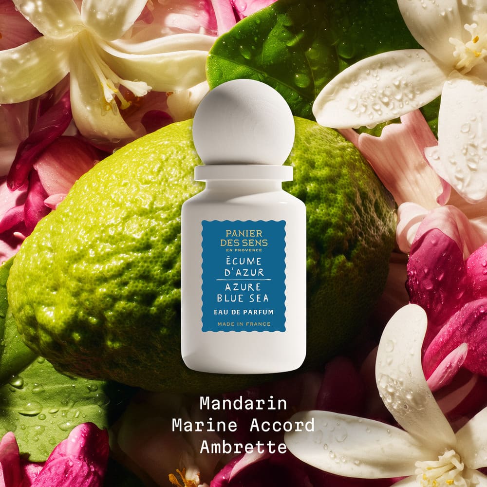 White perfume bottle with blue label on a background of green leaves and pink flowers