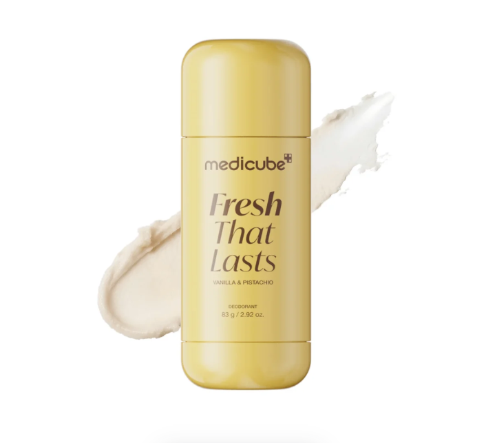 A yellow-green deodorant stick from the brand medicube, labeled 'Fresh That Lasts' in vanilla and pistachio, shown against a white background with a cream-colored product smear behind it.
